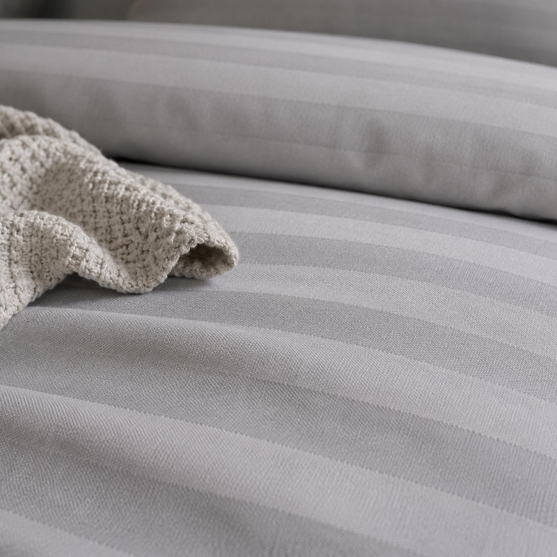 Gray striped bedding with a textured blanket on a bed