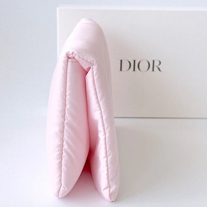 A light pink quilted pouch or clutch standing in front of a white Dior box on a clean white background.