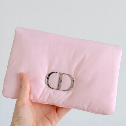 Pink clutch bag with a brand logo held by a hand against a light gray background