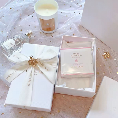 Guerlain skincare gift set featuring a boxed Aqua Alegrória treatment and a wrapped cream product tied with a branded ribbon, styled on a pink starry fabric surface with a candle and bottle nearby.
