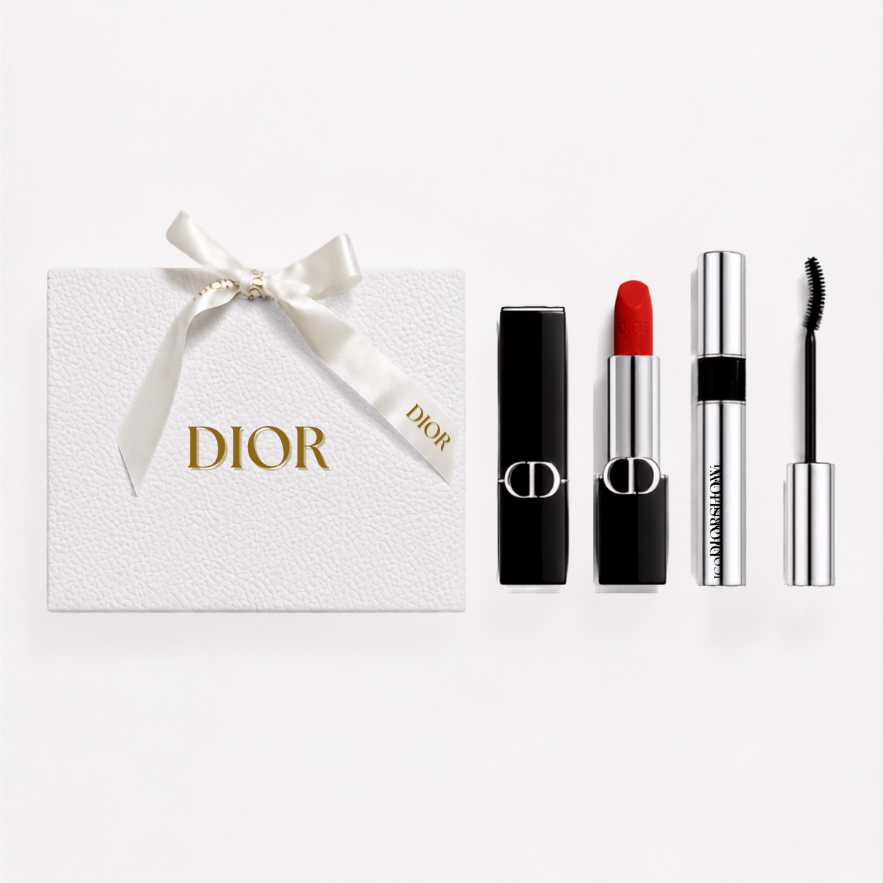 Dior gift set featuring a white textured Dior box with a white ribbon bow and gold logo, alongside a black lipstick with a red bullet, a silver mascara tube, and a black-and-silver eyeliner wand on a white background.