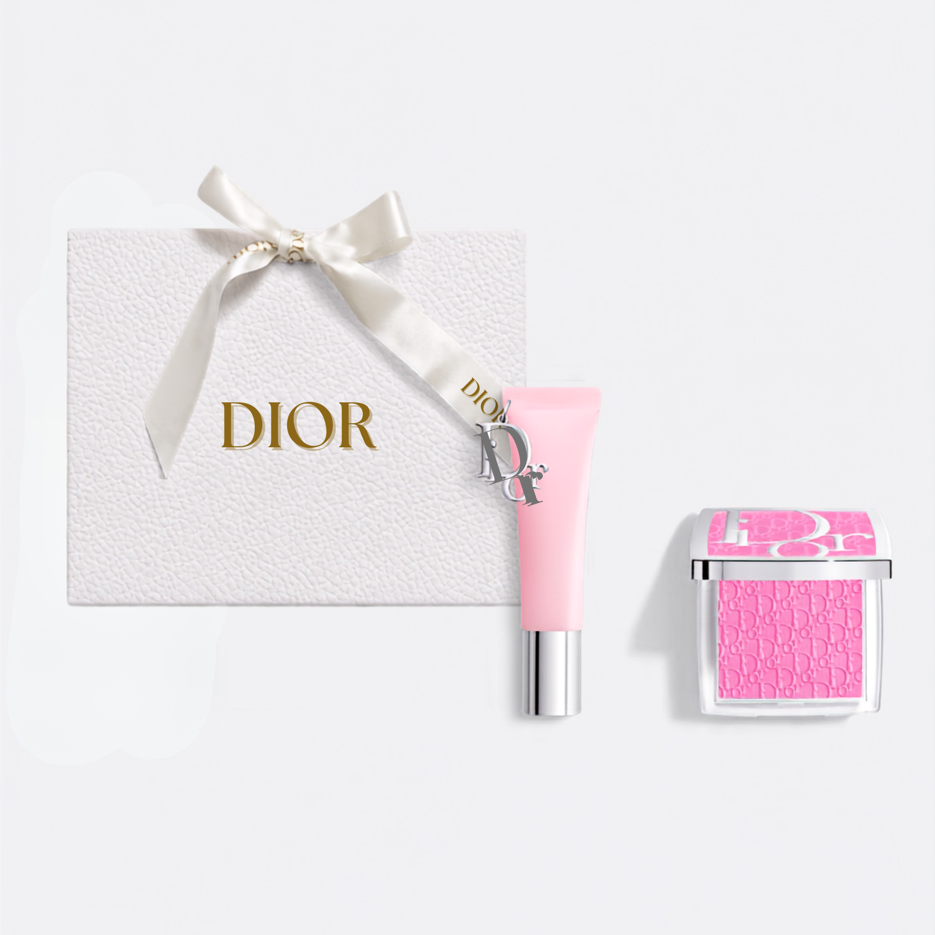 Dior gift set featuring a textured white box with a cream ribbon and gold DIOR logo, a light pink cream tube with a silver cap, and a pink square compact with a clear lid.