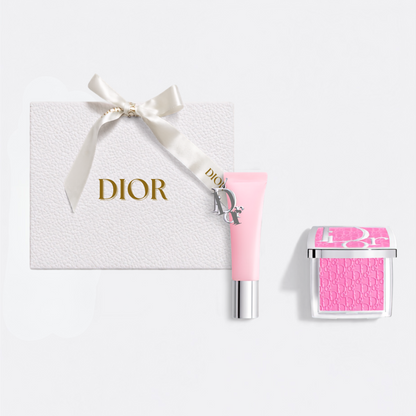 Dior gift set featuring a textured white box with a cream ribbon and gold DIOR logo, a light pink cream tube with a silver cap, and a pink square compact with a clear lid.