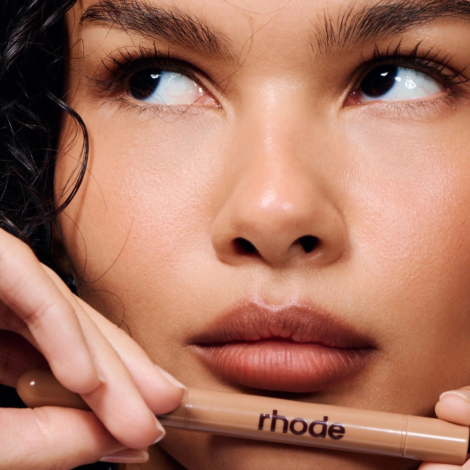 Close-up of a person holding a cosmetic product with 'rhode' branding.