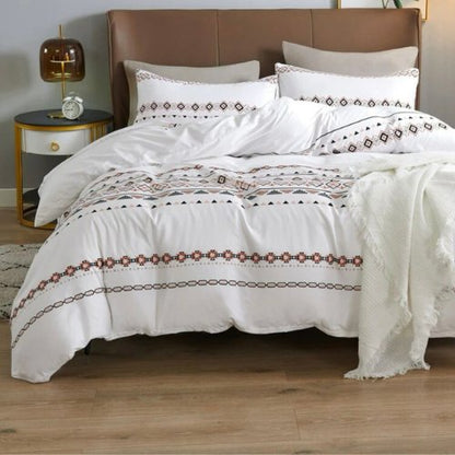 A white bedding set with geometric patterns on the duvet cover and pillowcases, displayed on a bed with a wooden headboard. A nightstand with a lamp and a book is visible to the left. United Arab Emirates, Abu Dhabi